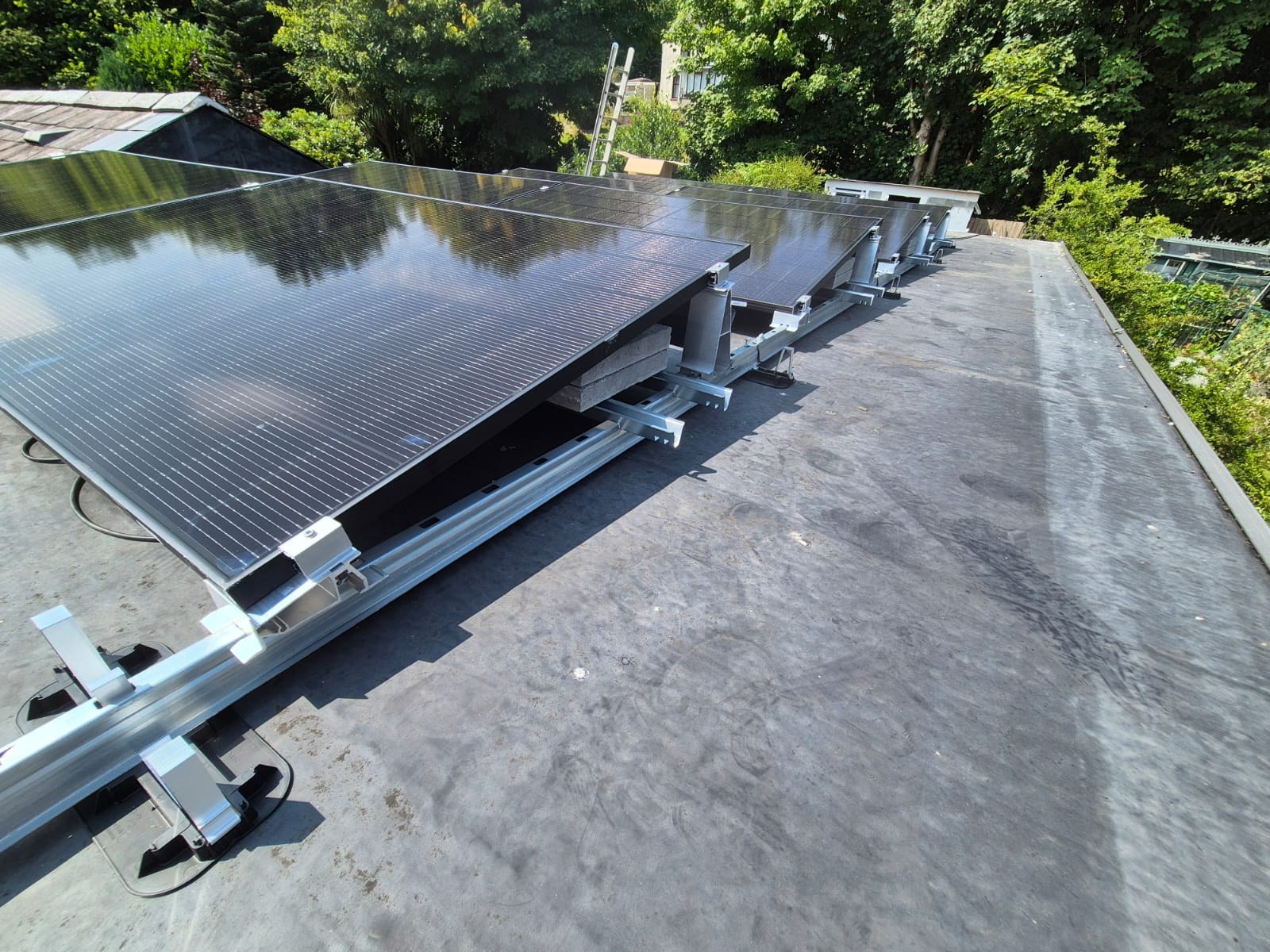 Solar panels on a ballasted aluminium mounting frame on a flat rubber roof, with concrete weights holding the frame in place.