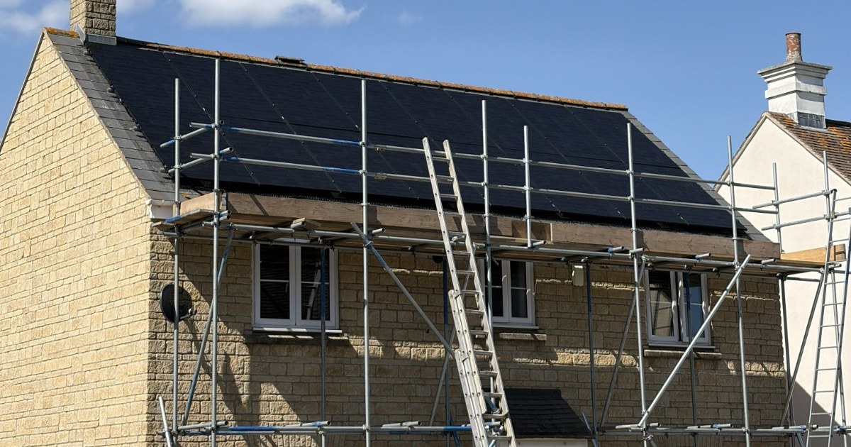 Stone-built home in Wiltshire with all-black solar panels on the roof behind scaffolding.