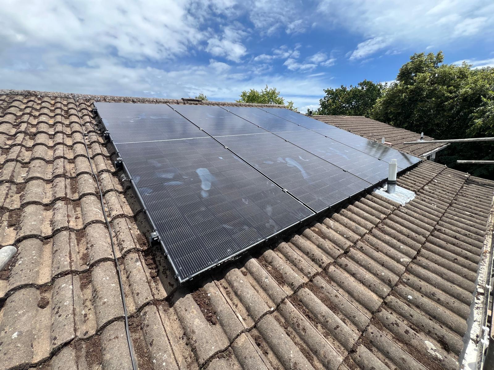 Eight all-black solar panels on a brown tiled pitched roof under a blue sky at a Southampton installation.