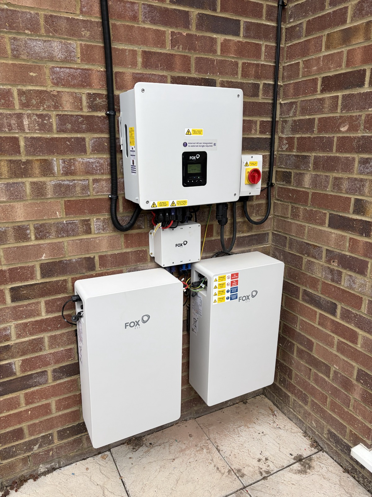 Fox ESS inverter and two home battery units installed on a brick wall by Cozy Home Solutions.