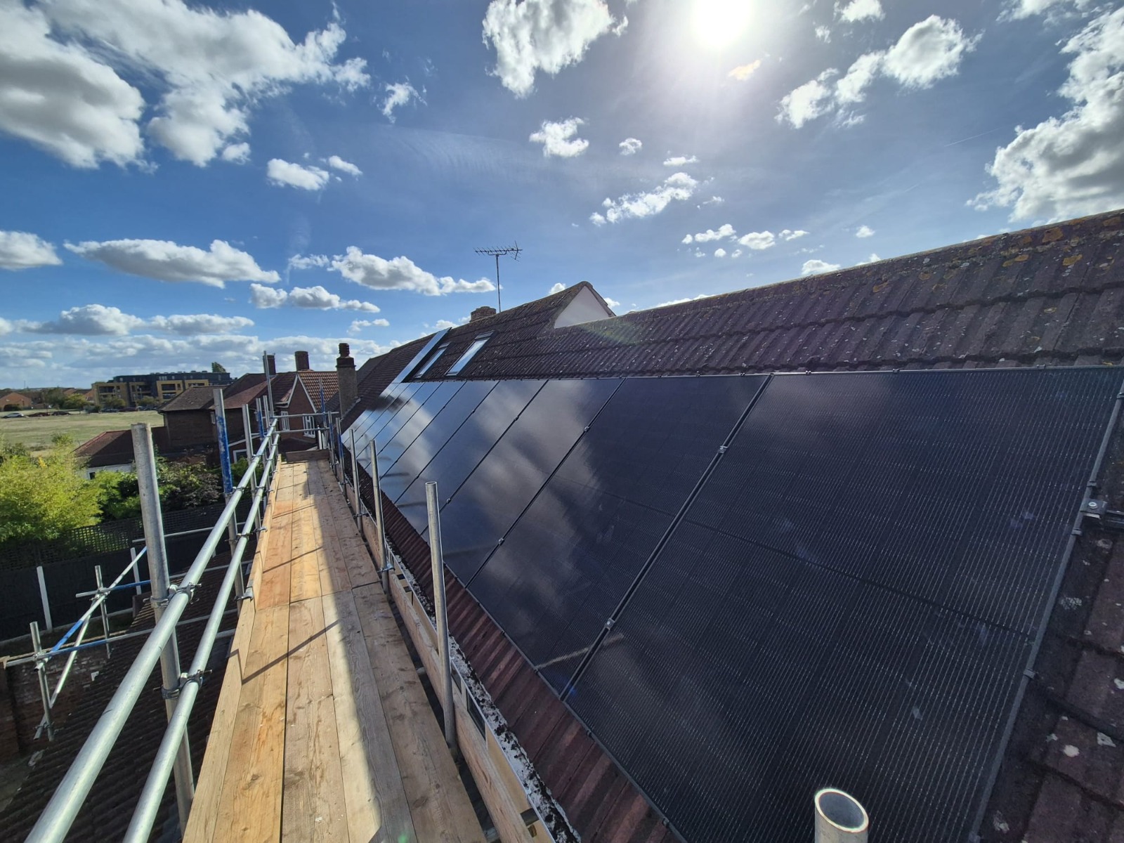 Rooftop solar panel array beside a scaffold walkway on a tiled pitched roof, photographed by Cozy Home Solutions.