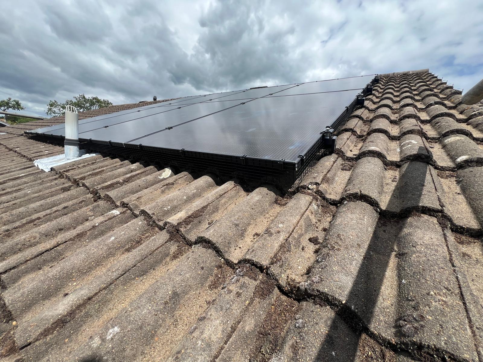 Low view along a tiled roof showing black bird mesh fitted beneath the edge of the solar panels.