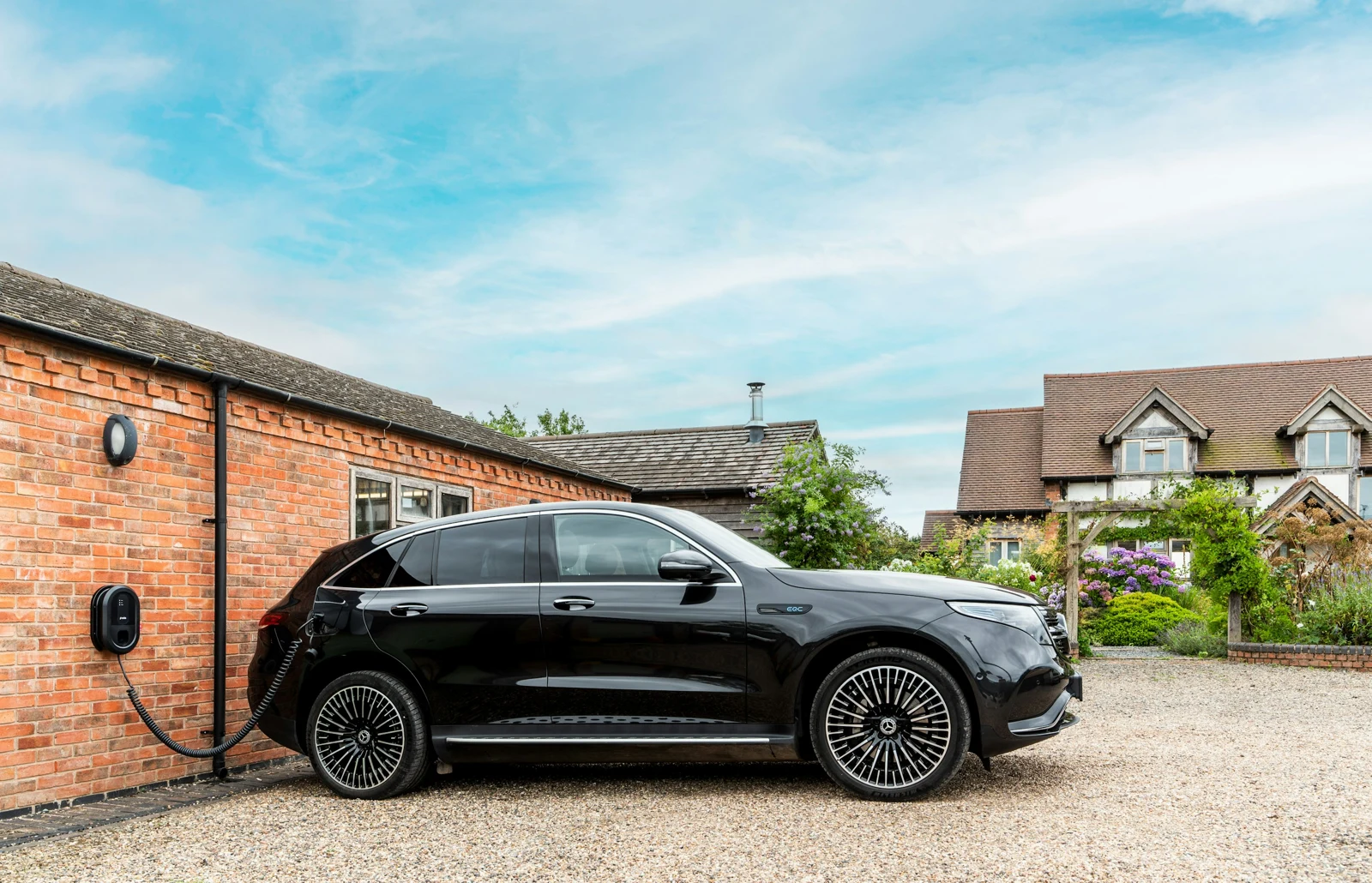 A wall mounted EV charge point on a house with a car on the driveway
