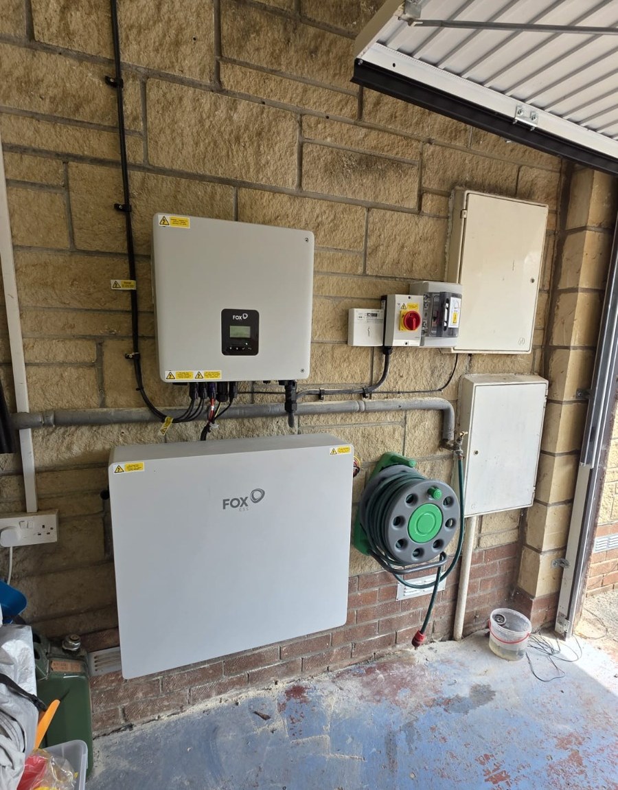 Fox ESS inverter and wall-mounted battery storage unit on a stone garage wall, wired into the household electrics.